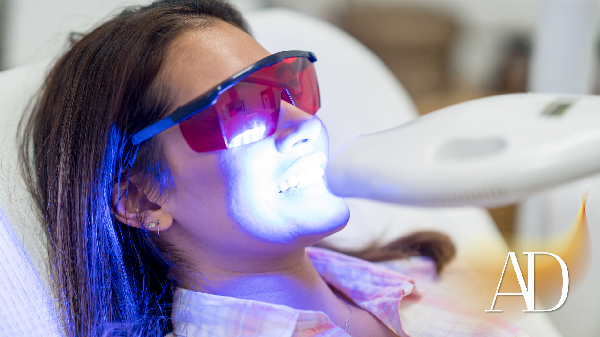 A woman is getting a teeth whitening treatment at a dental office.