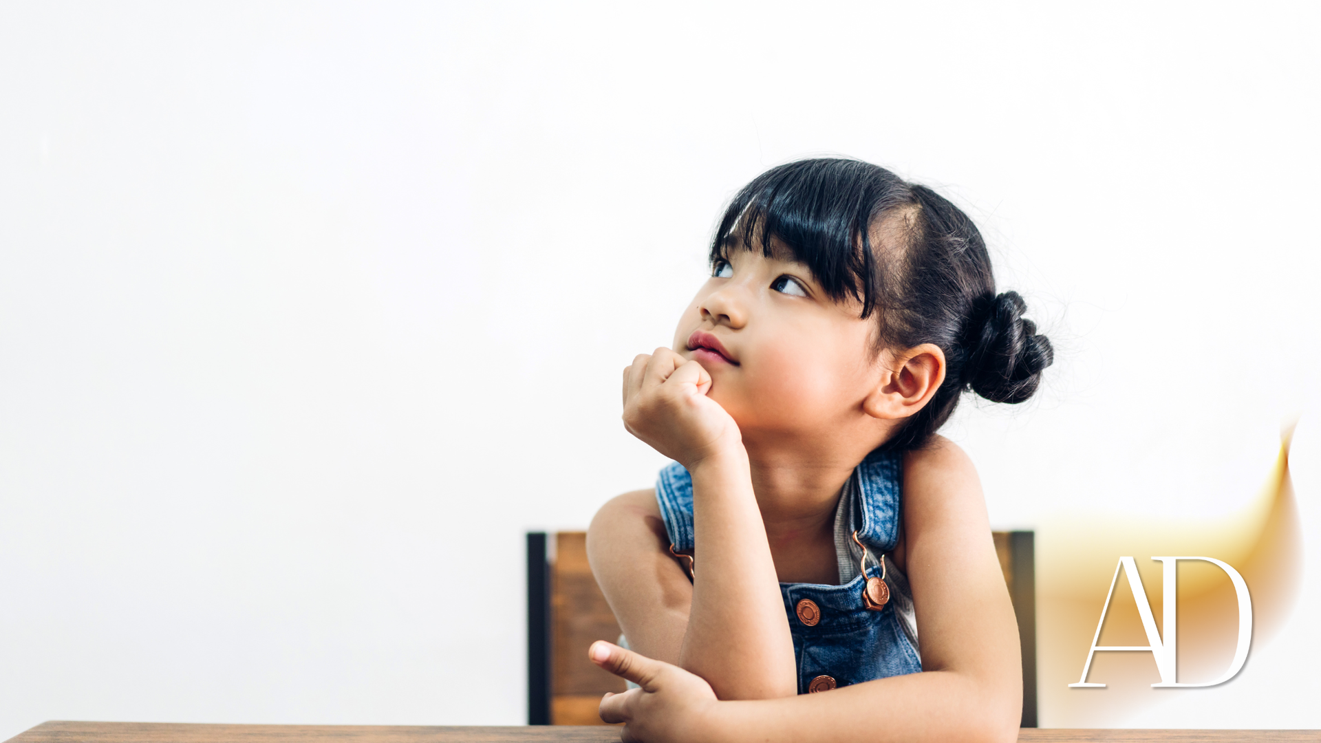 Young child with a thoughtful expression, resting chin on hand, looking upward.