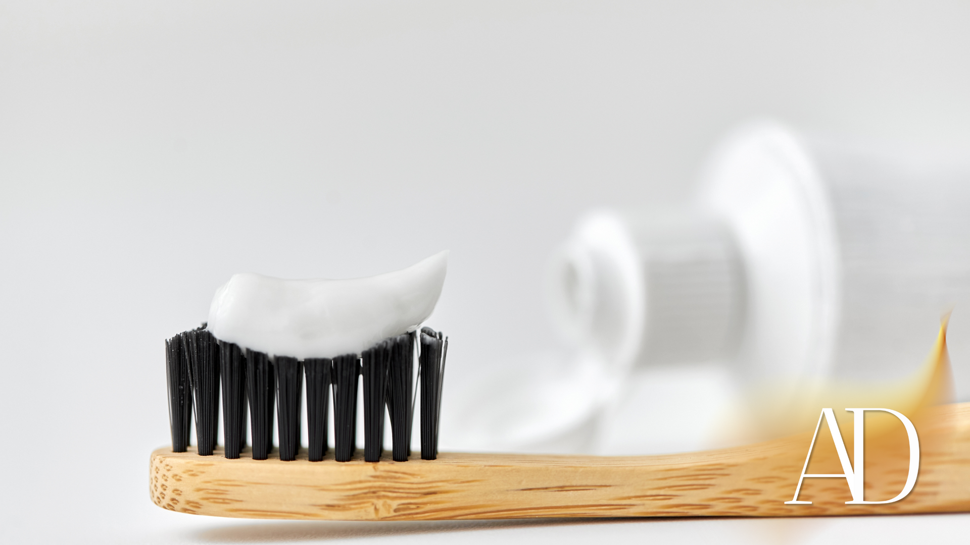 A wooden toothbrush with toothpaste on it and a tube of toothpaste behind it.