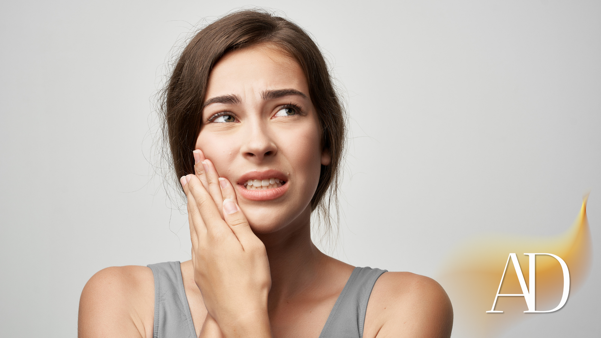 Woman with pained expression, touching her cheek as if experiencing a toothache.
