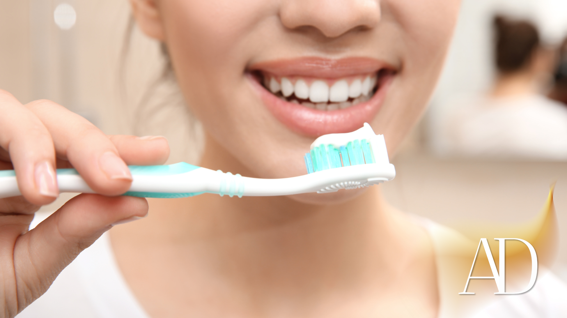 Woman smiling, holding a toothbrush with toothpaste in a bathroom.