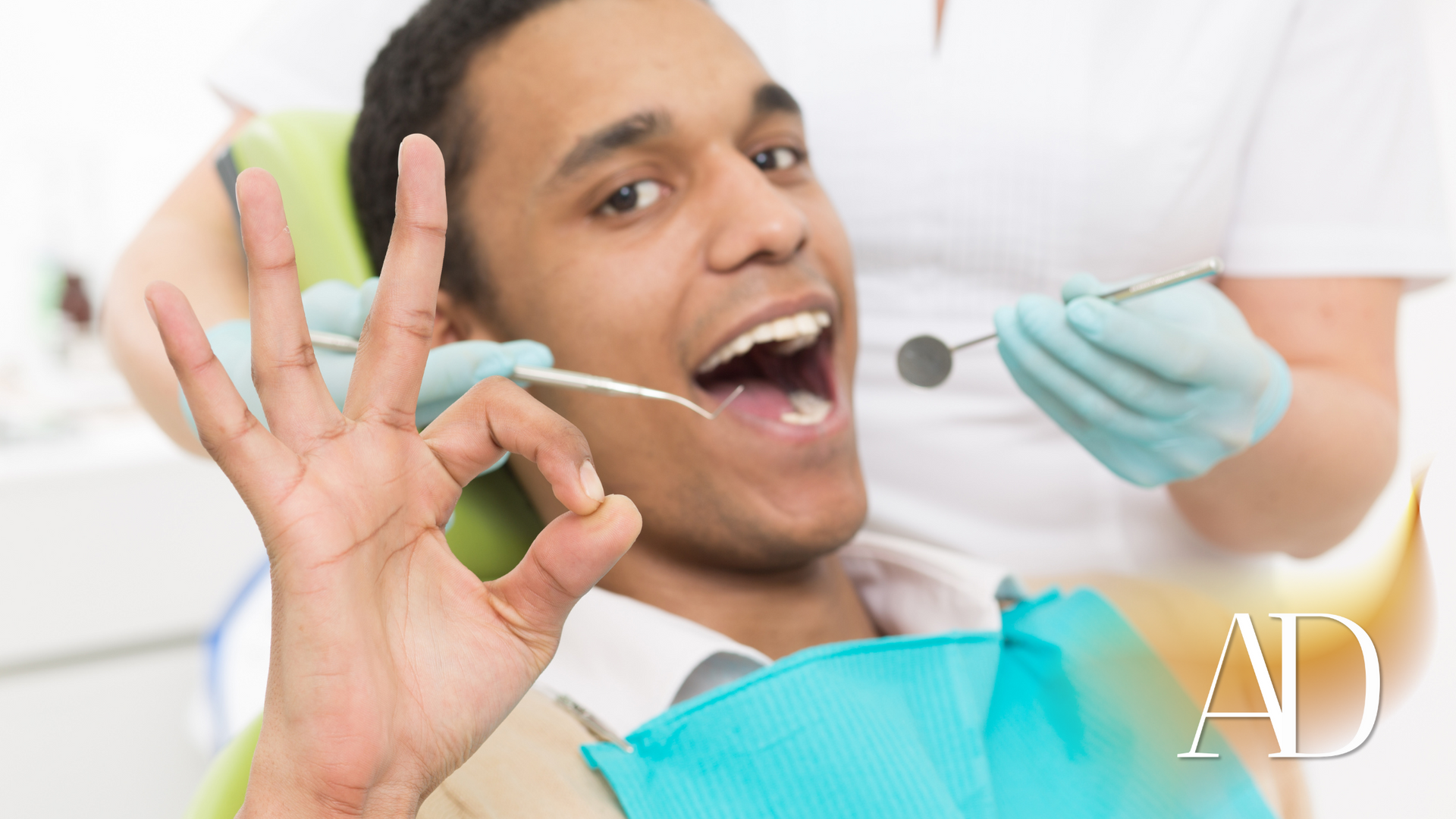 A man is sitting in a dental chair giving an okay sign.