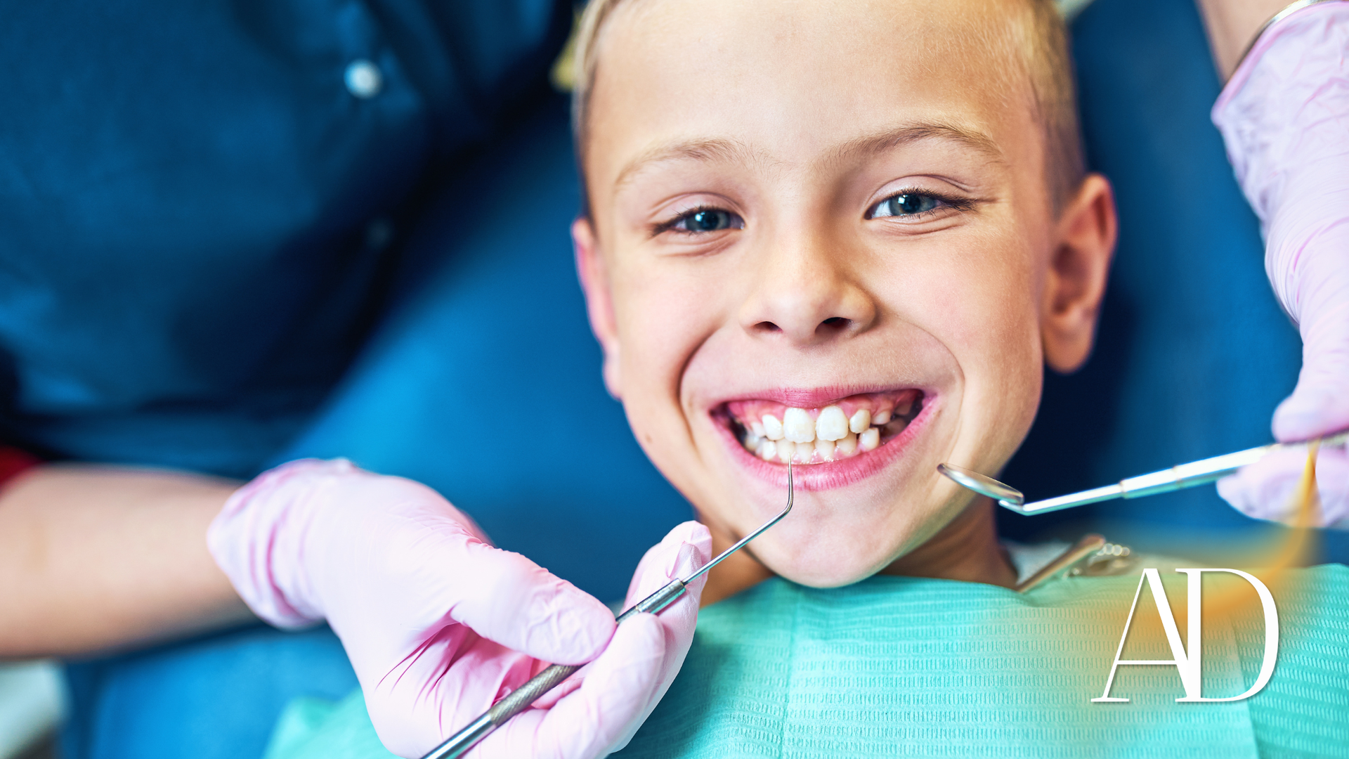 Boy smiling at the dentist during a check-up. Dentist's gloved hands hold tools.