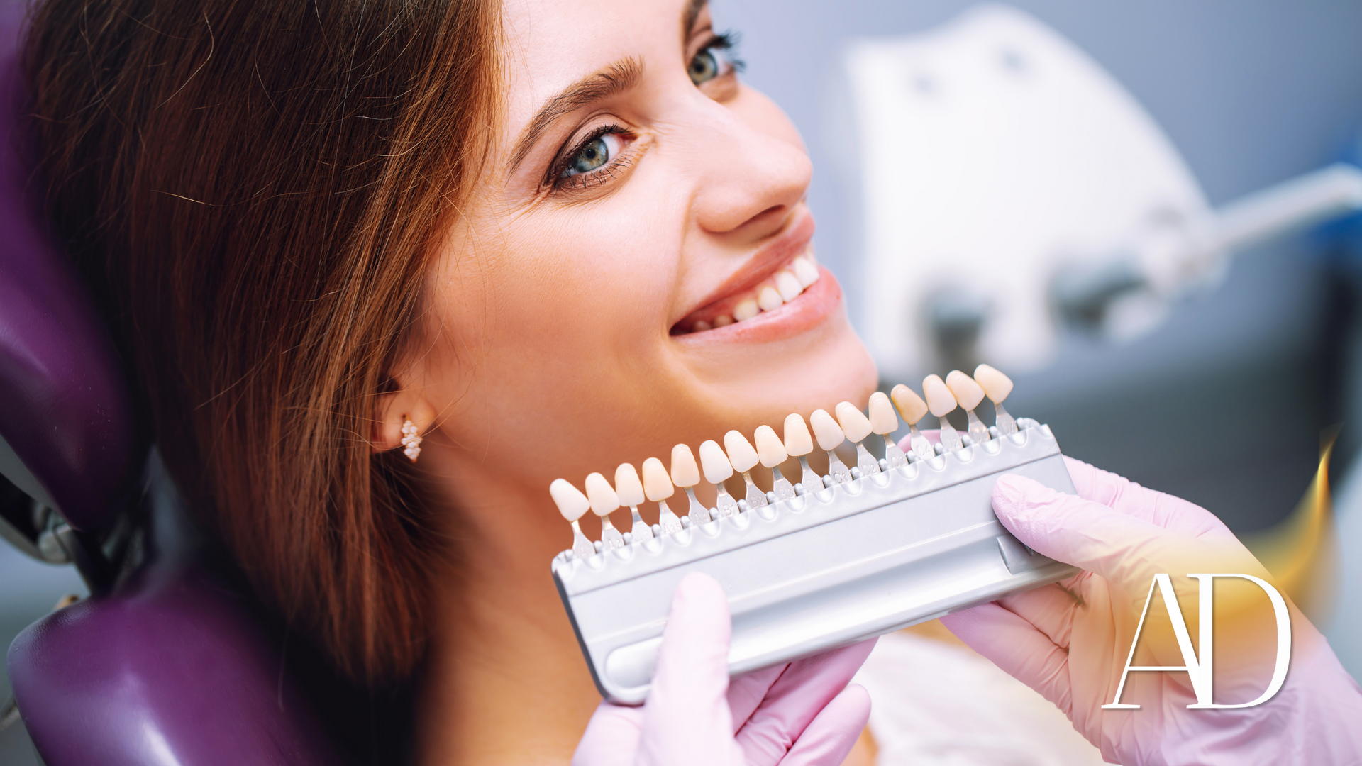 A woman is sitting in a dental chair while a dentist holds a tooth color chart.