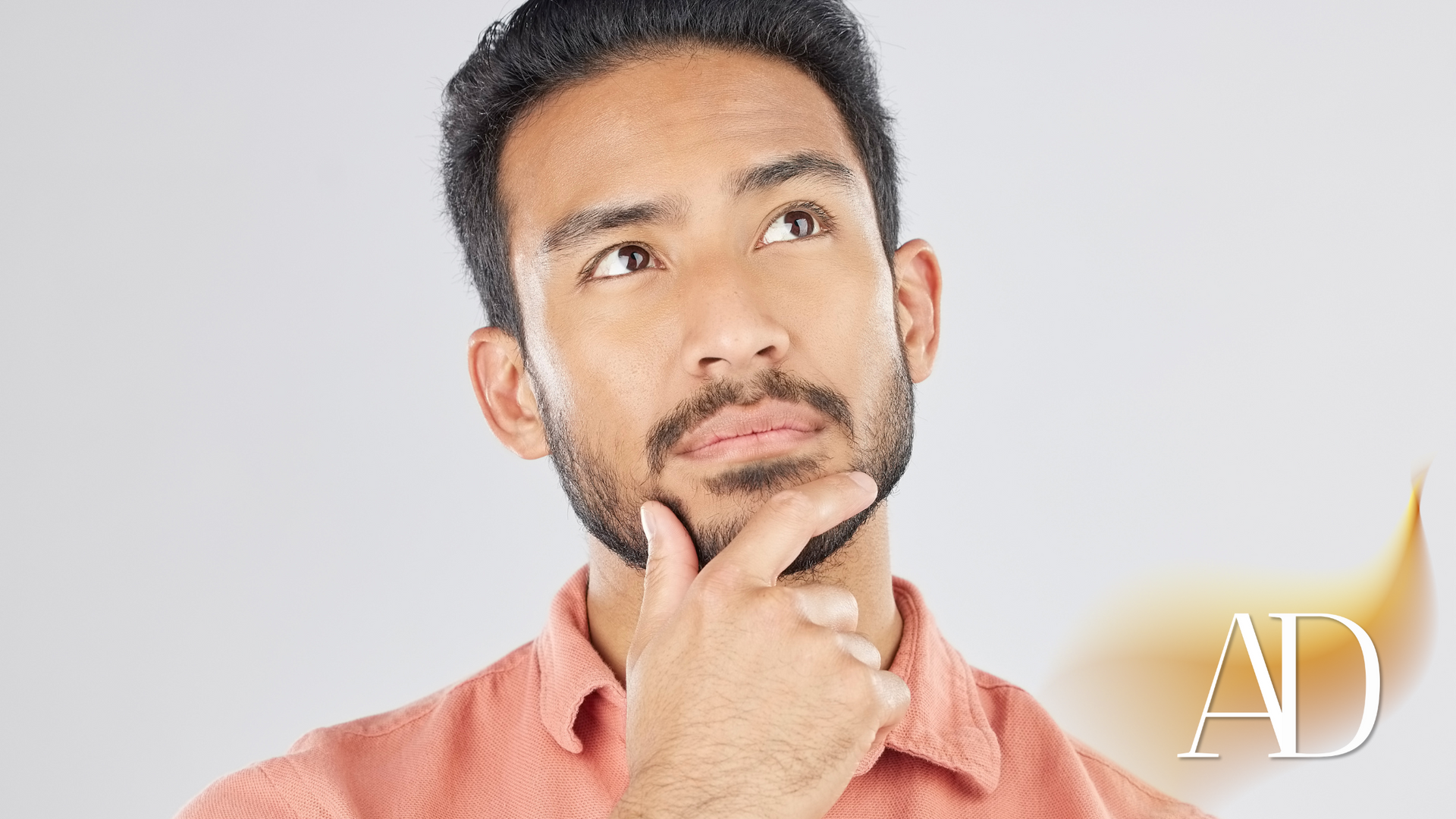 A man with a beard is thinking with his hand on his chin.