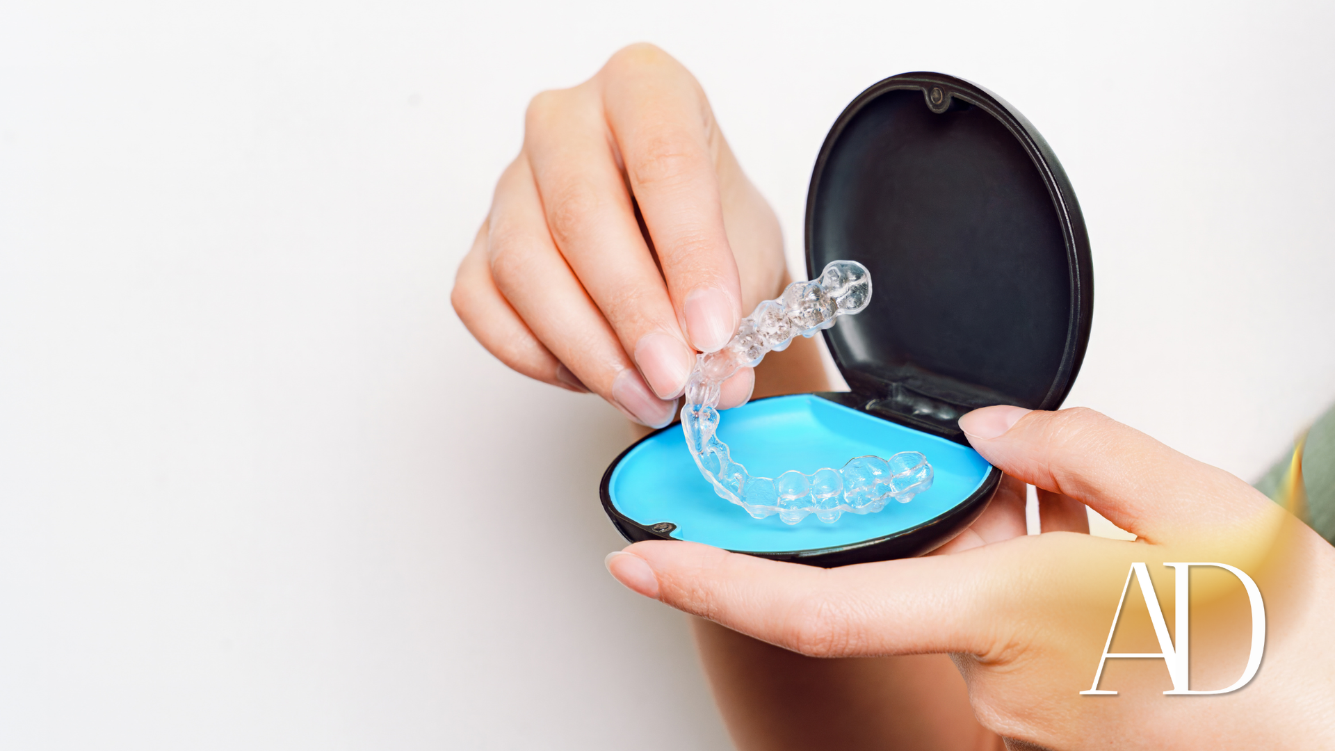 Person removing clear aligner from a blue case, against a white backdrop.