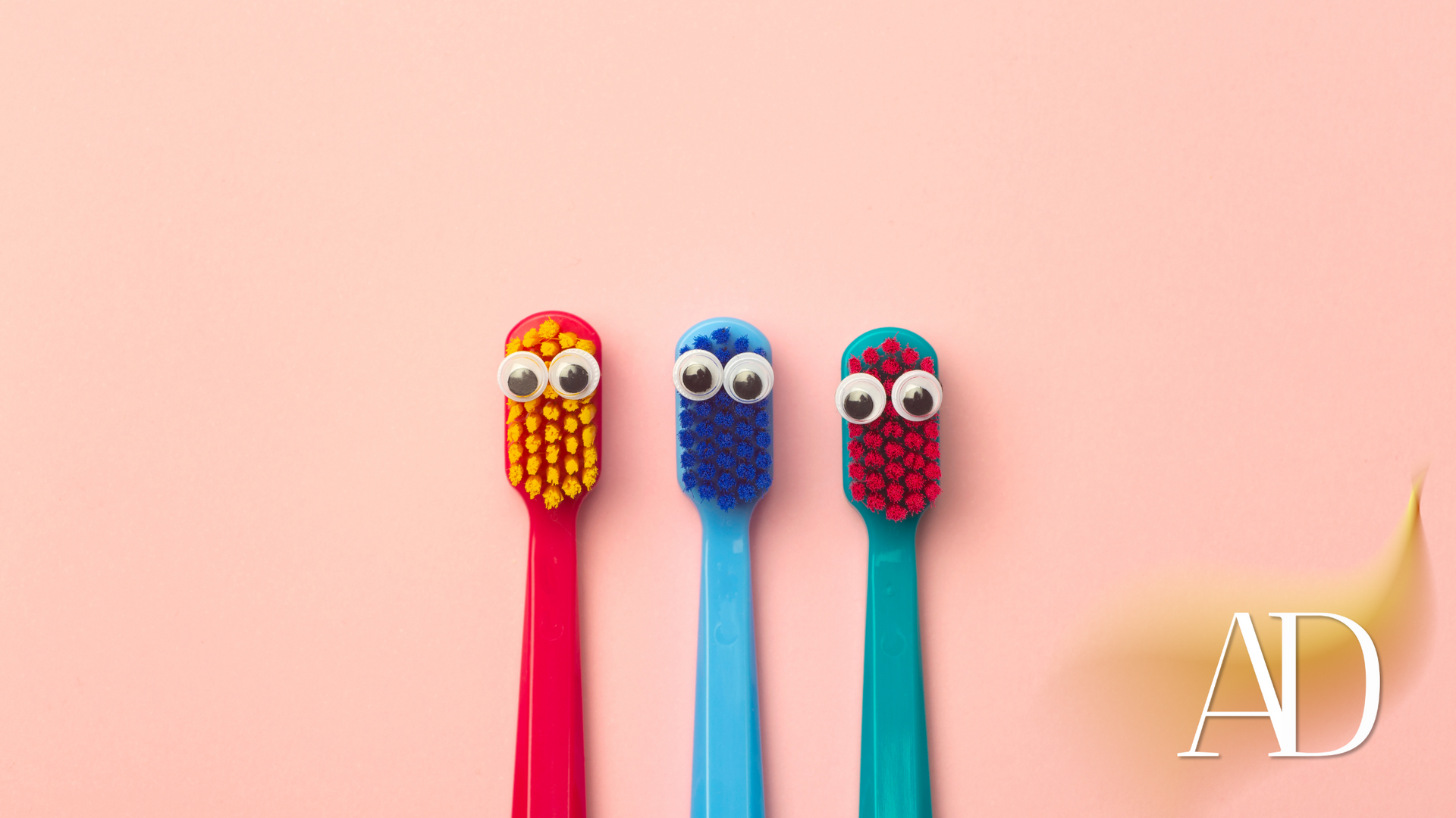 Three toothbrushes with googly eyes on them on a pink background.