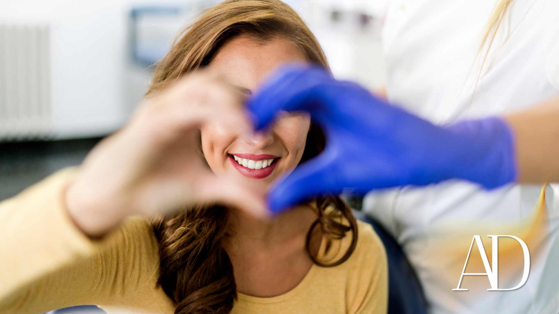 A woman is making a heart shape with her hands in a dental office.