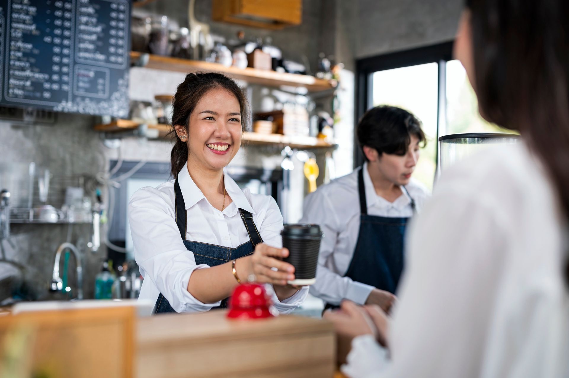 Barista serving a cup of coffee to a customer in a cafe counter.