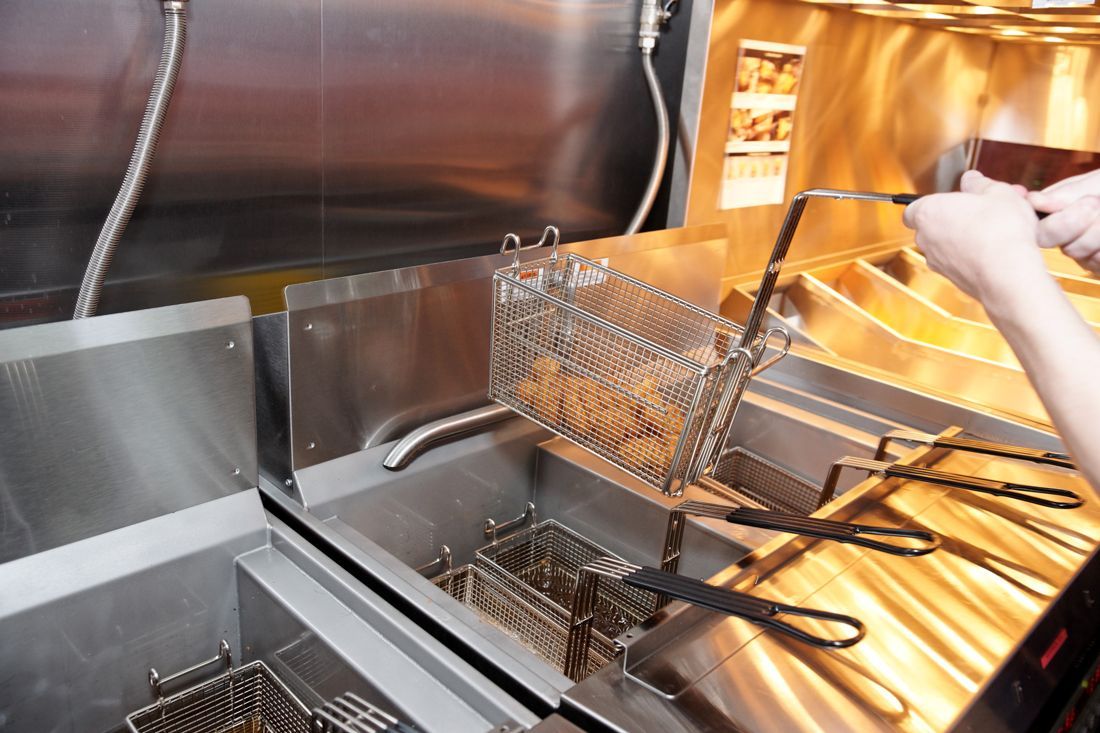 A person is cooking chicken in a deep fryer.