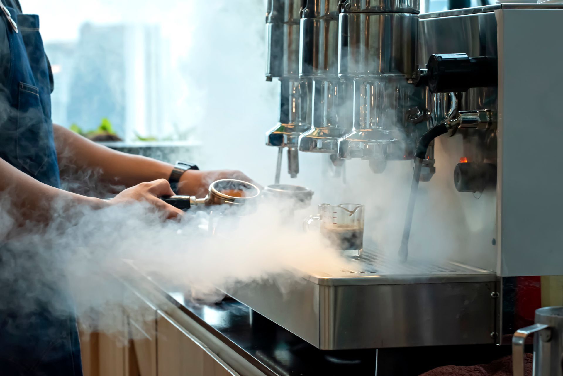 Barista makes coffee with espresso machine, surrounded by steam.