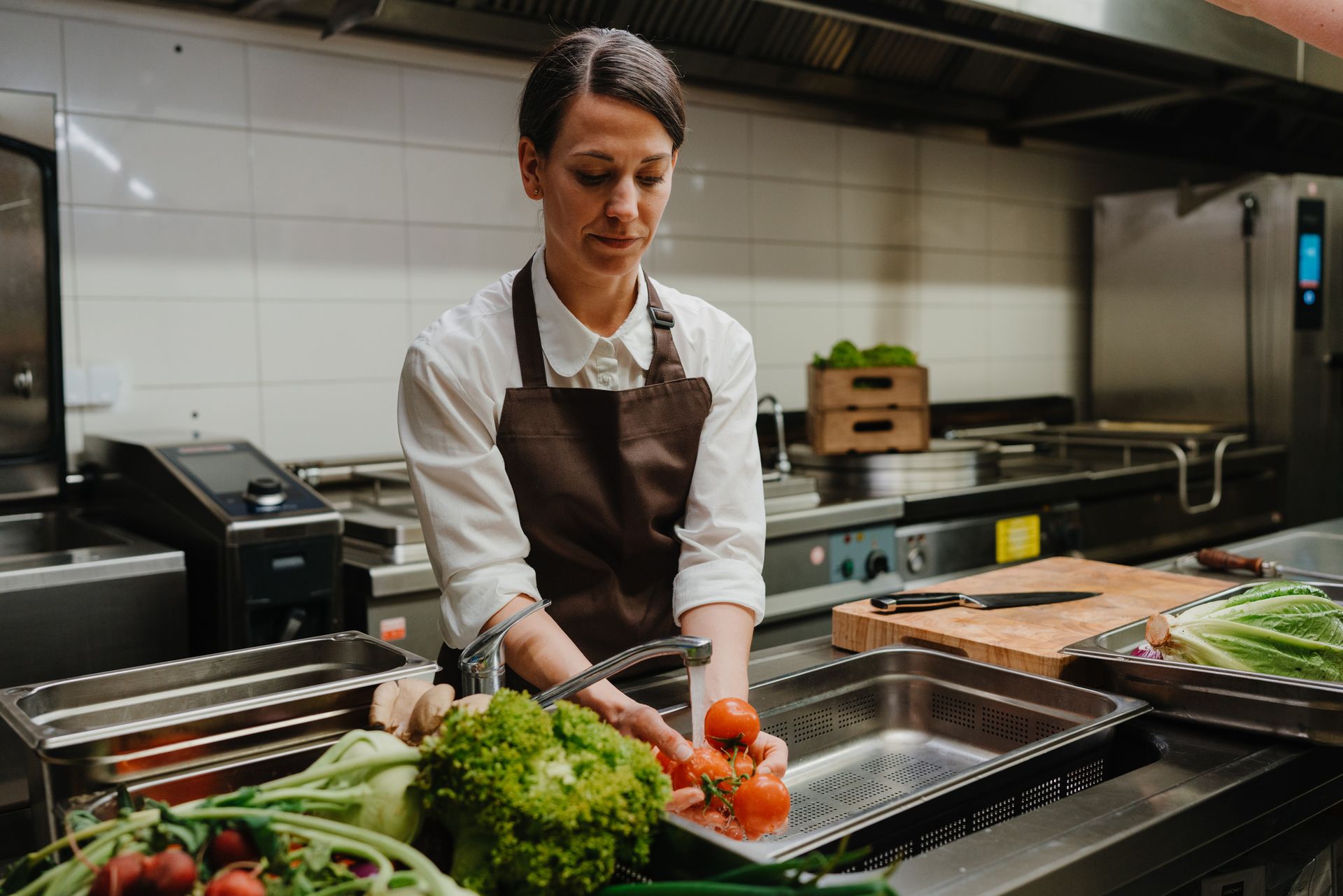 Woman in restaurant kitchen washing fresh vegetable.