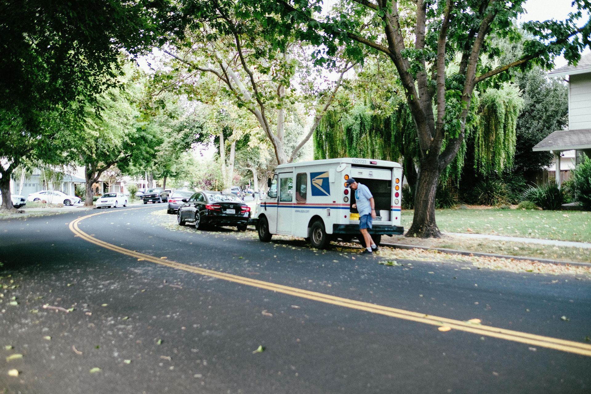 White utility truck on a tree-lined street with parked cars and a person standing beside it