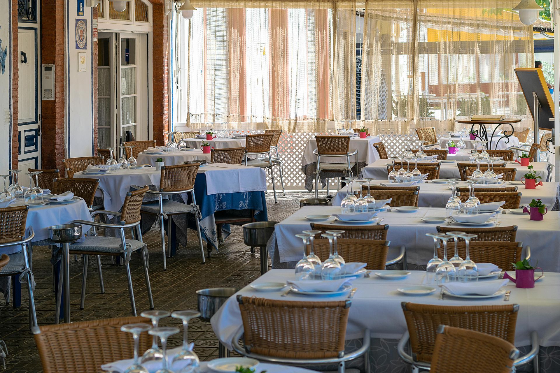 Outdoor café dining area with white-clothed tables and woven chairs under a covered patio
