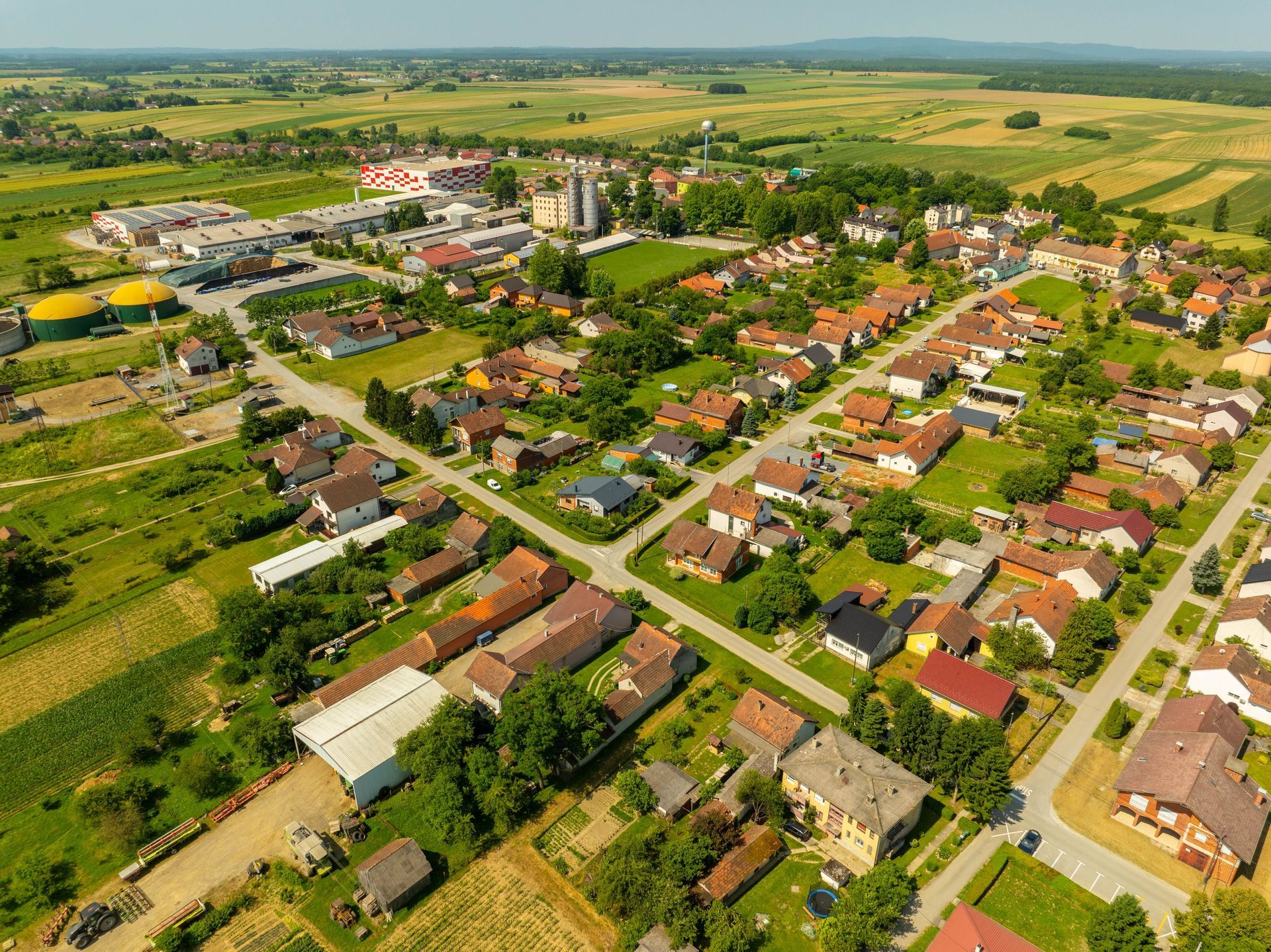 Aerial view of a small village with houses, roads, and green farmland under a clear sky