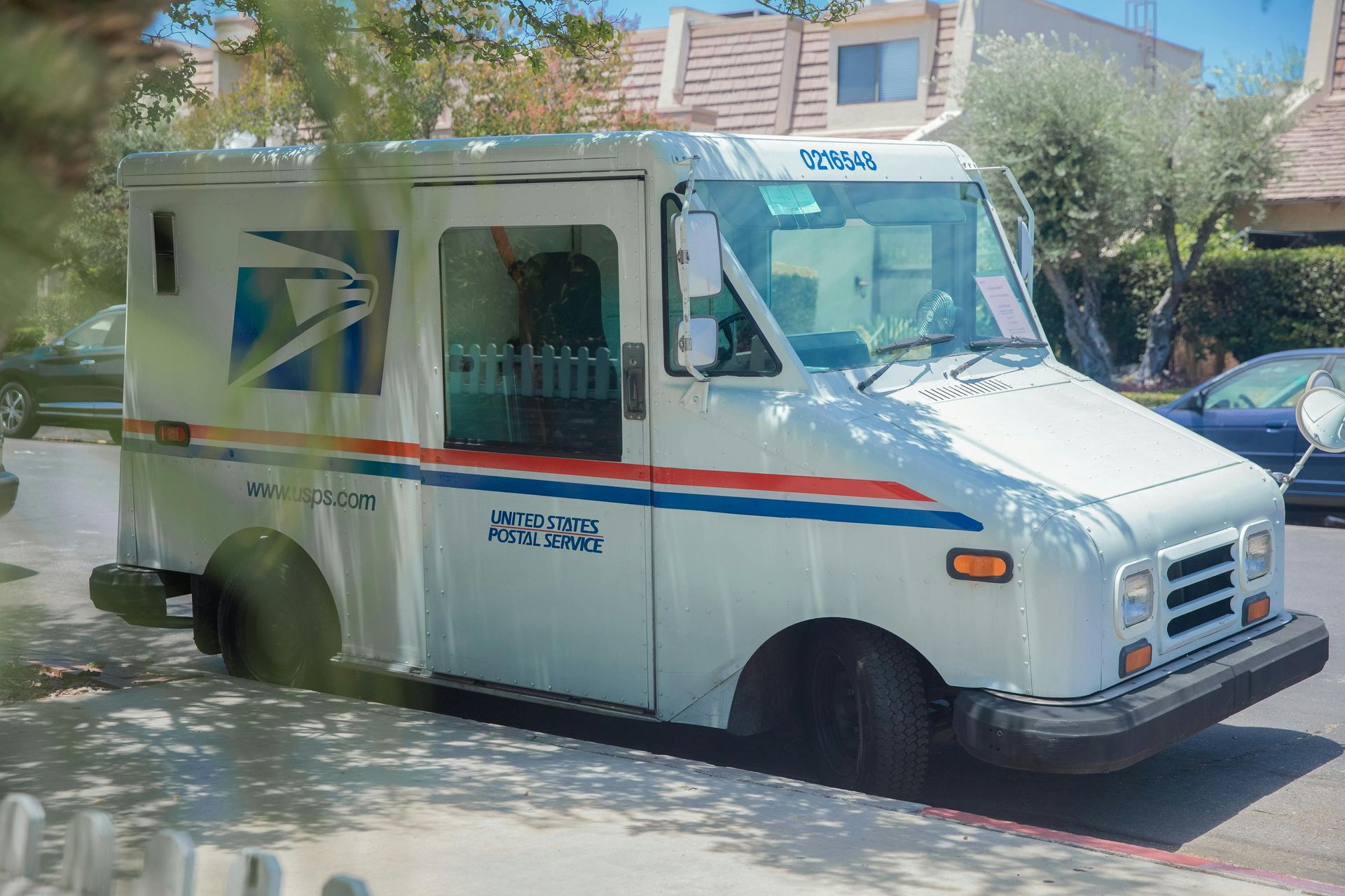 White delivery truck parked on a sunny street, with blue and red stripes and a side logo panel.