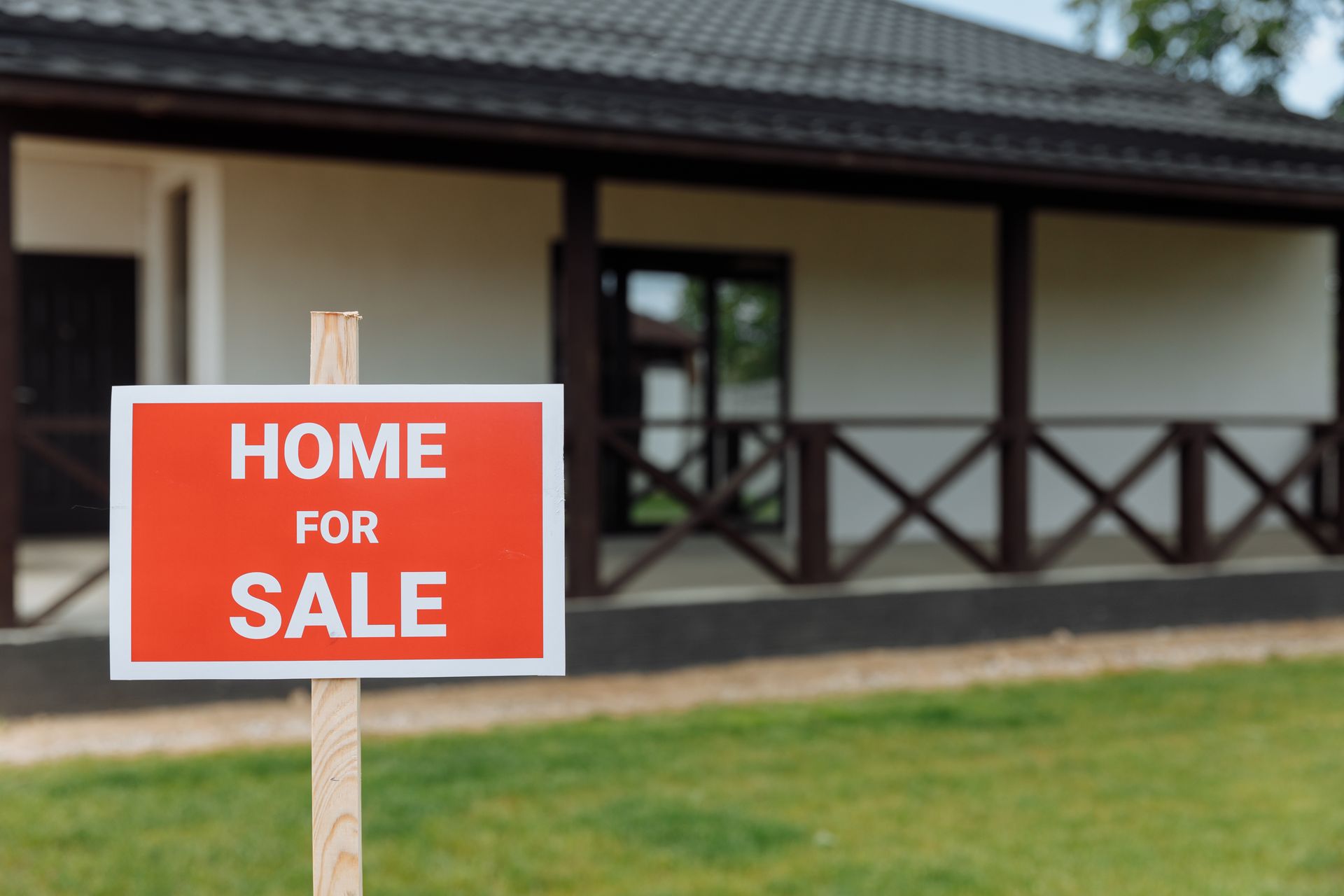 Red “Home for Sale” sign in front of a house with a porch and lawn.