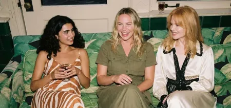 Tres mujeres sentadas en un sofá, sonriendo y charlando en una sala de estar.