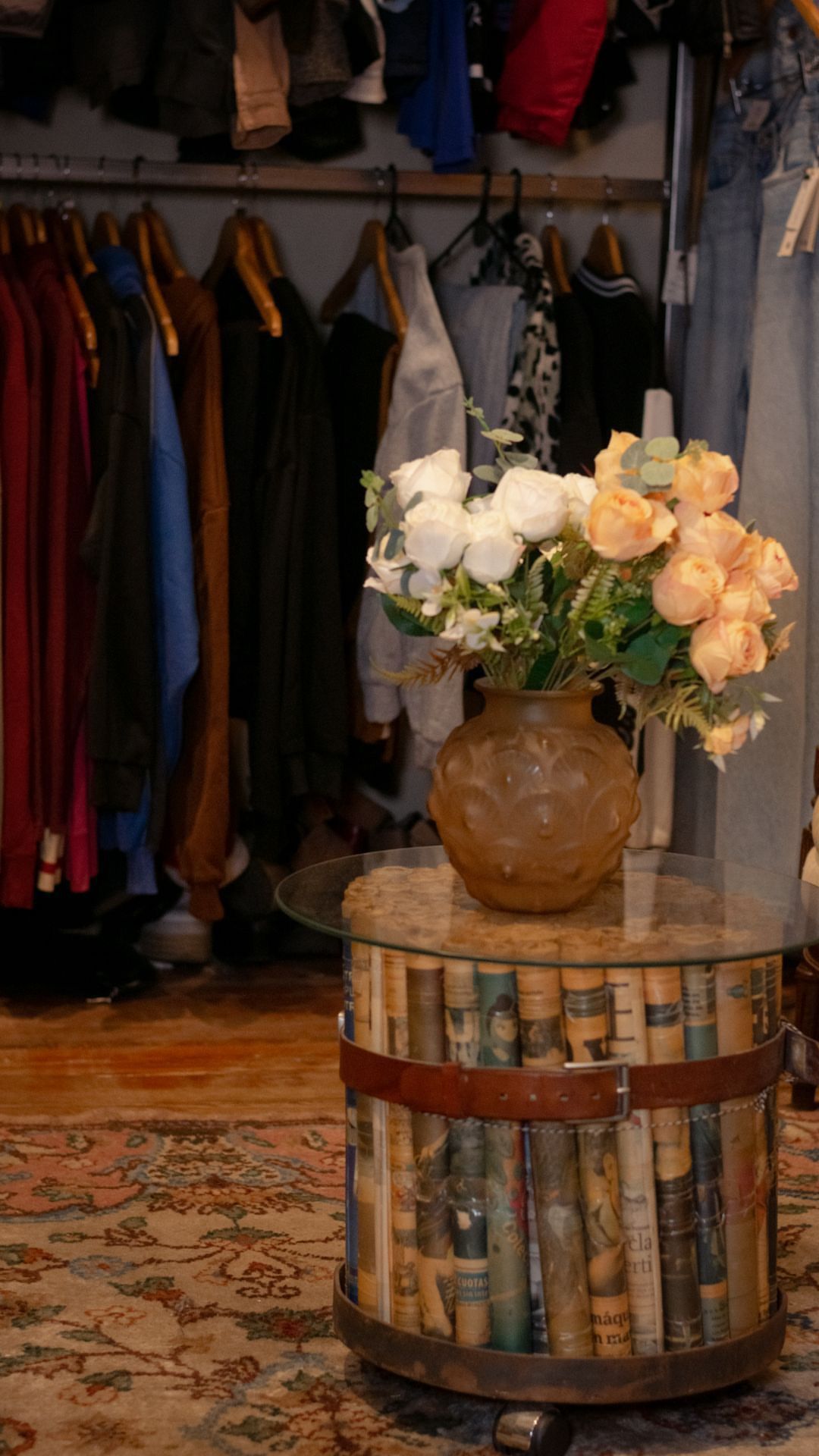 Mesa de barril de estilo vintage con un jarrón de flores blancas y color melocotón en una boutique con ropa colgada.