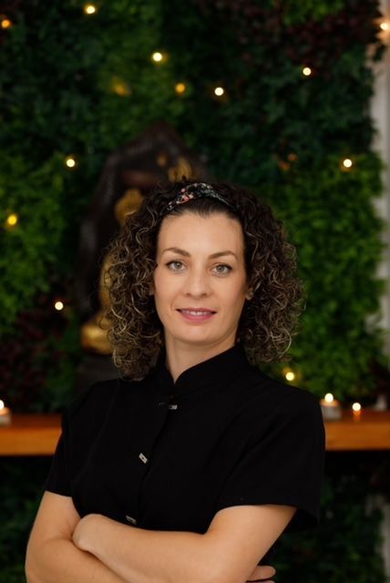 Una mujer con una camisa negra está parada con los brazos cruzados frente a una pared verde.