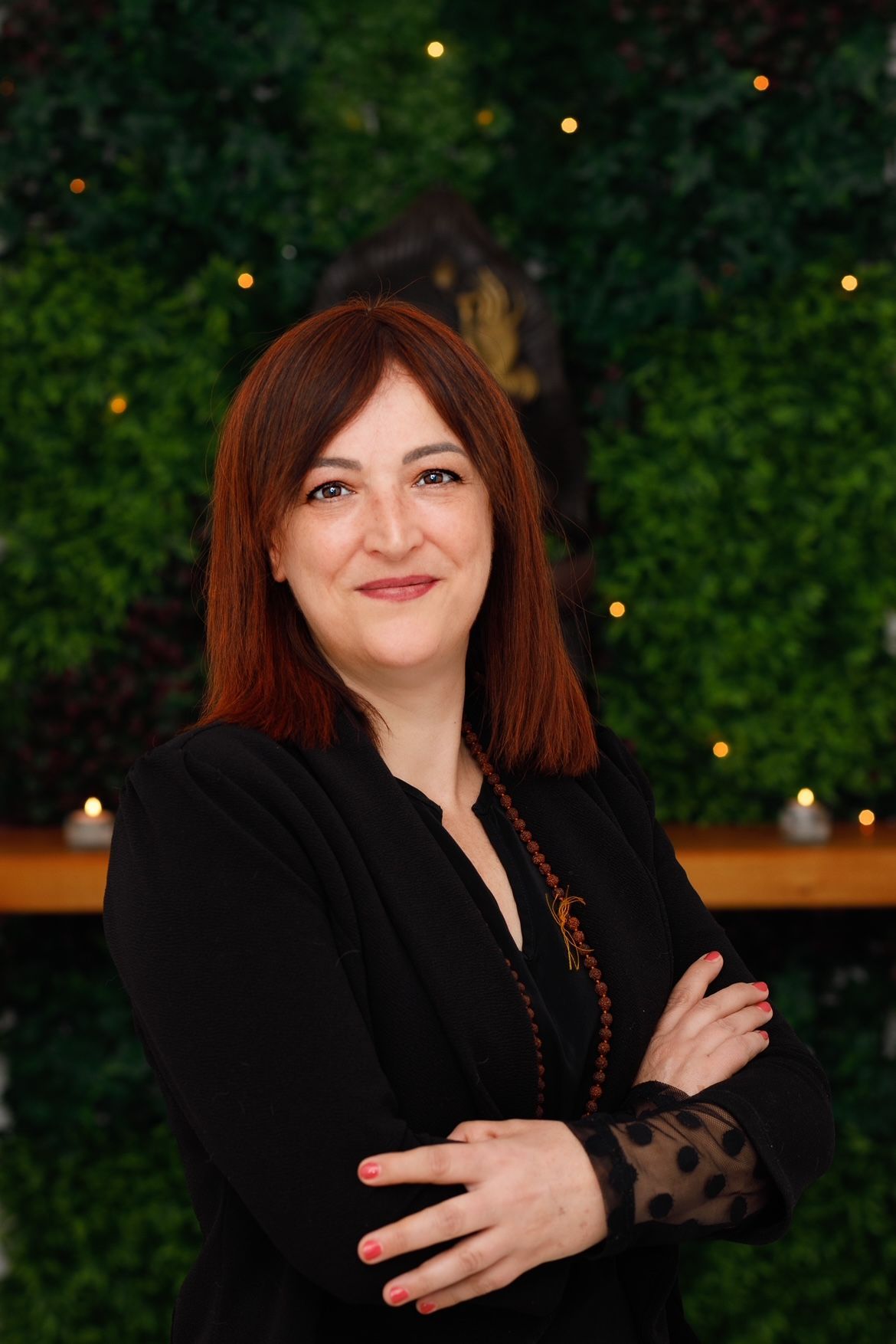 Una mujer con cabello rojo está parada frente a una pared verde con los brazos cruzados.