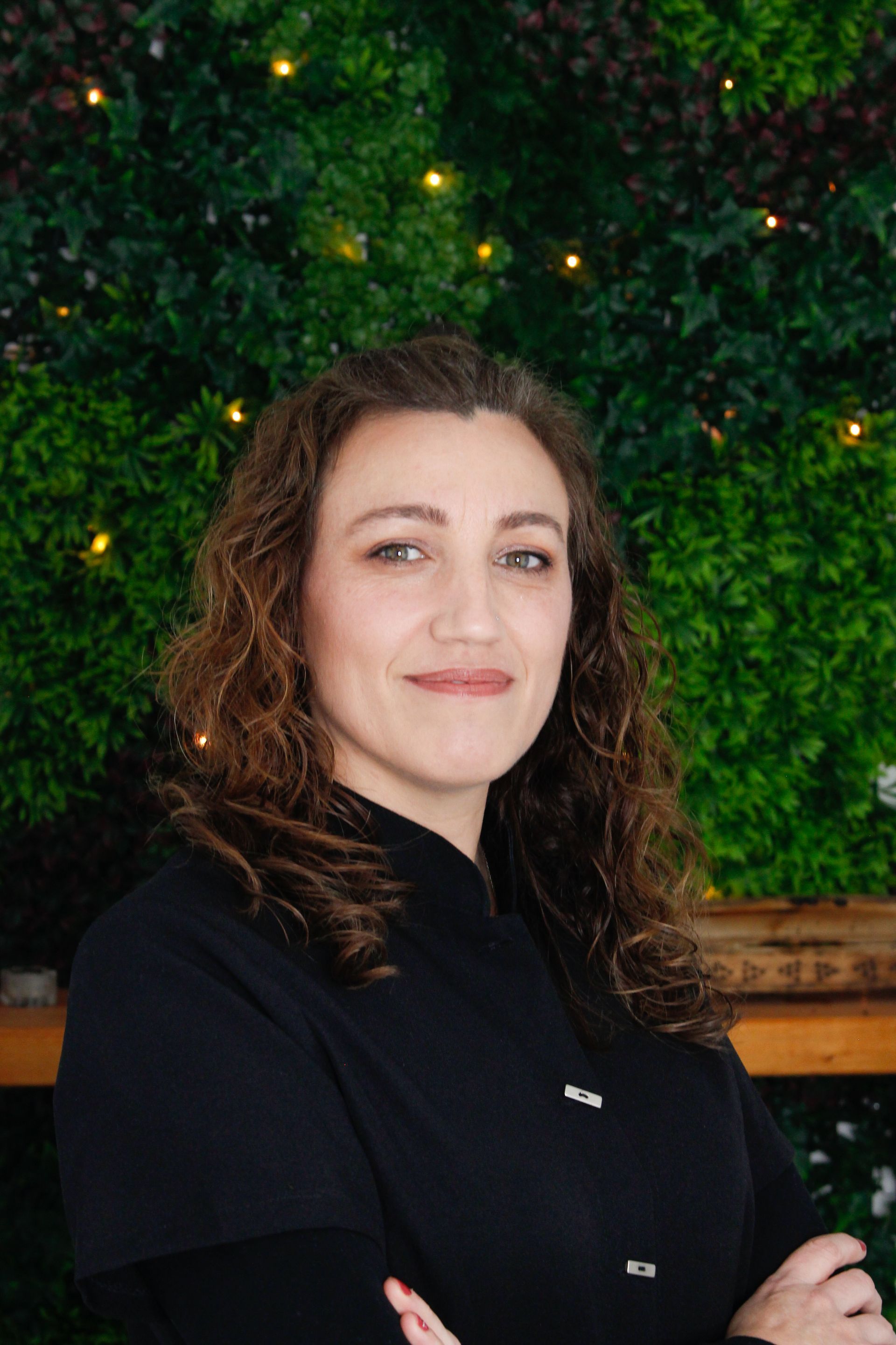 Una mujer está parada frente a una pared verde con los brazos cruzados.