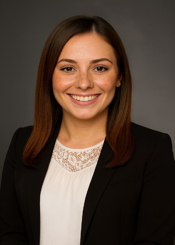 Woman in black blazer smiles, white top with lace, medium brown hair, grey background.