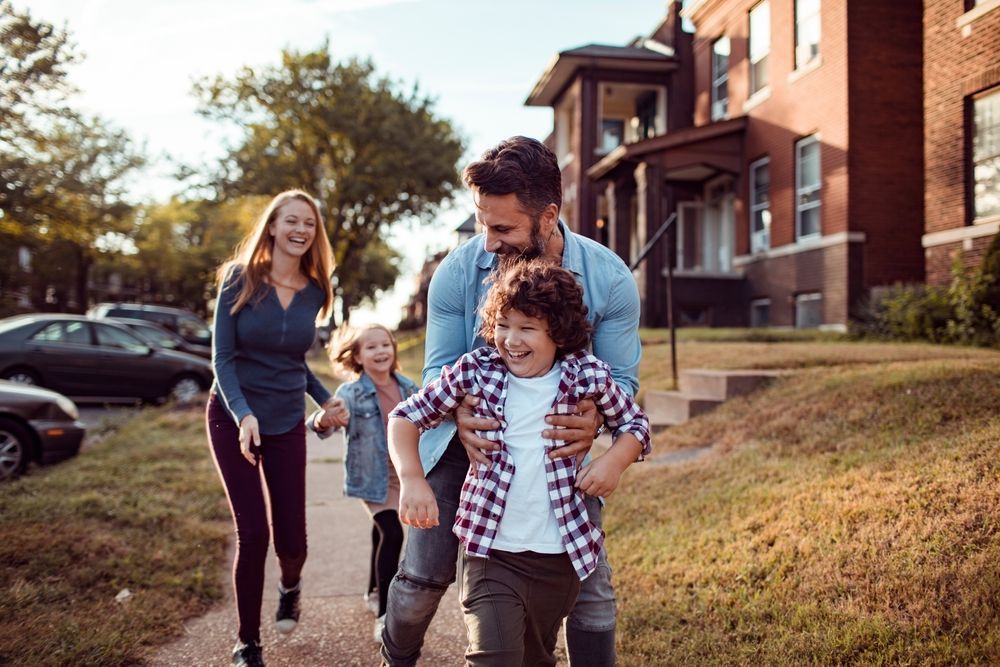 Family indoors making a roof with their hands, smiling.