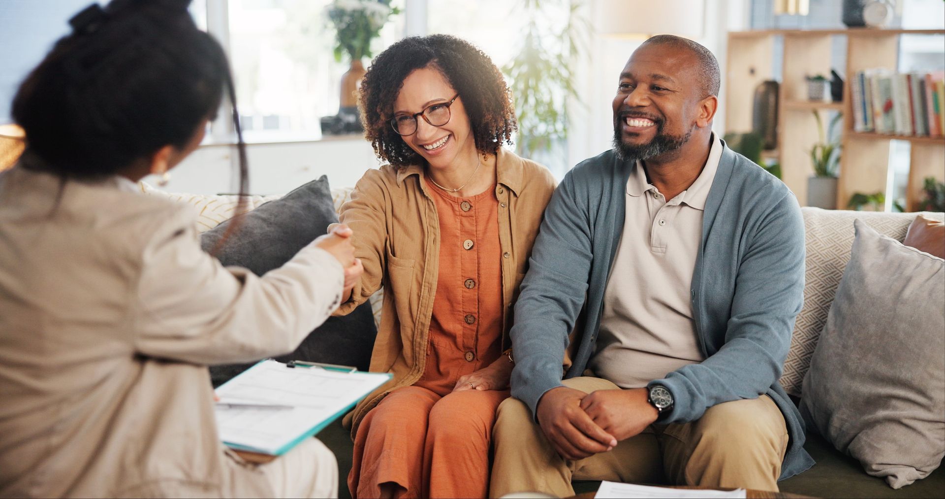 A financial advisor shakes hands with a smiling couple on a couch.