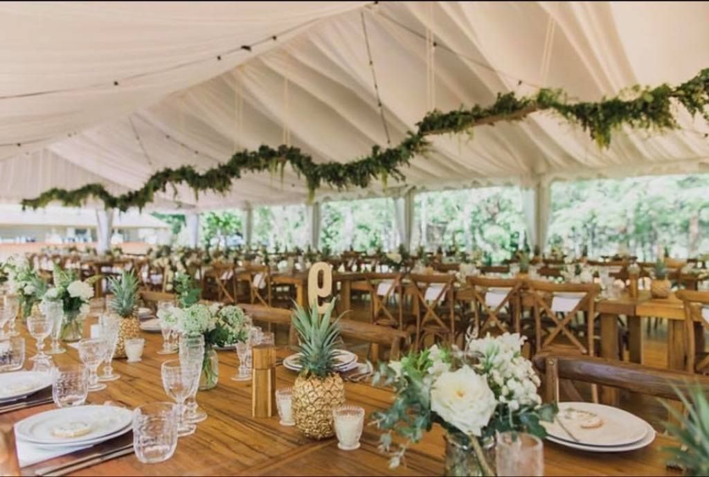 A long wooden table with pineapples and flowers on it under a tent.