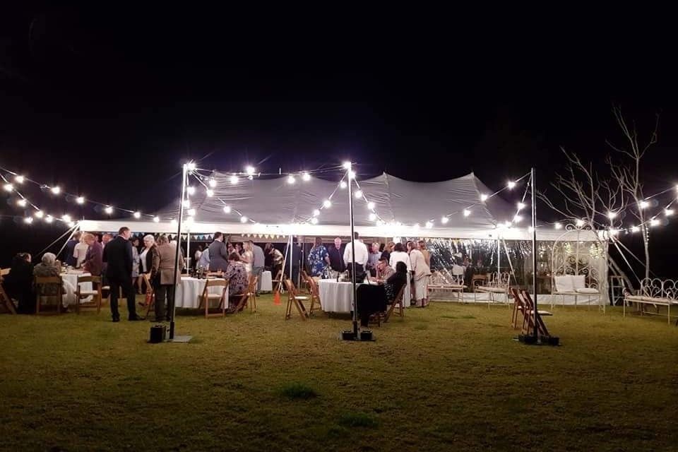 A group of people are standing outside of a tent at night.