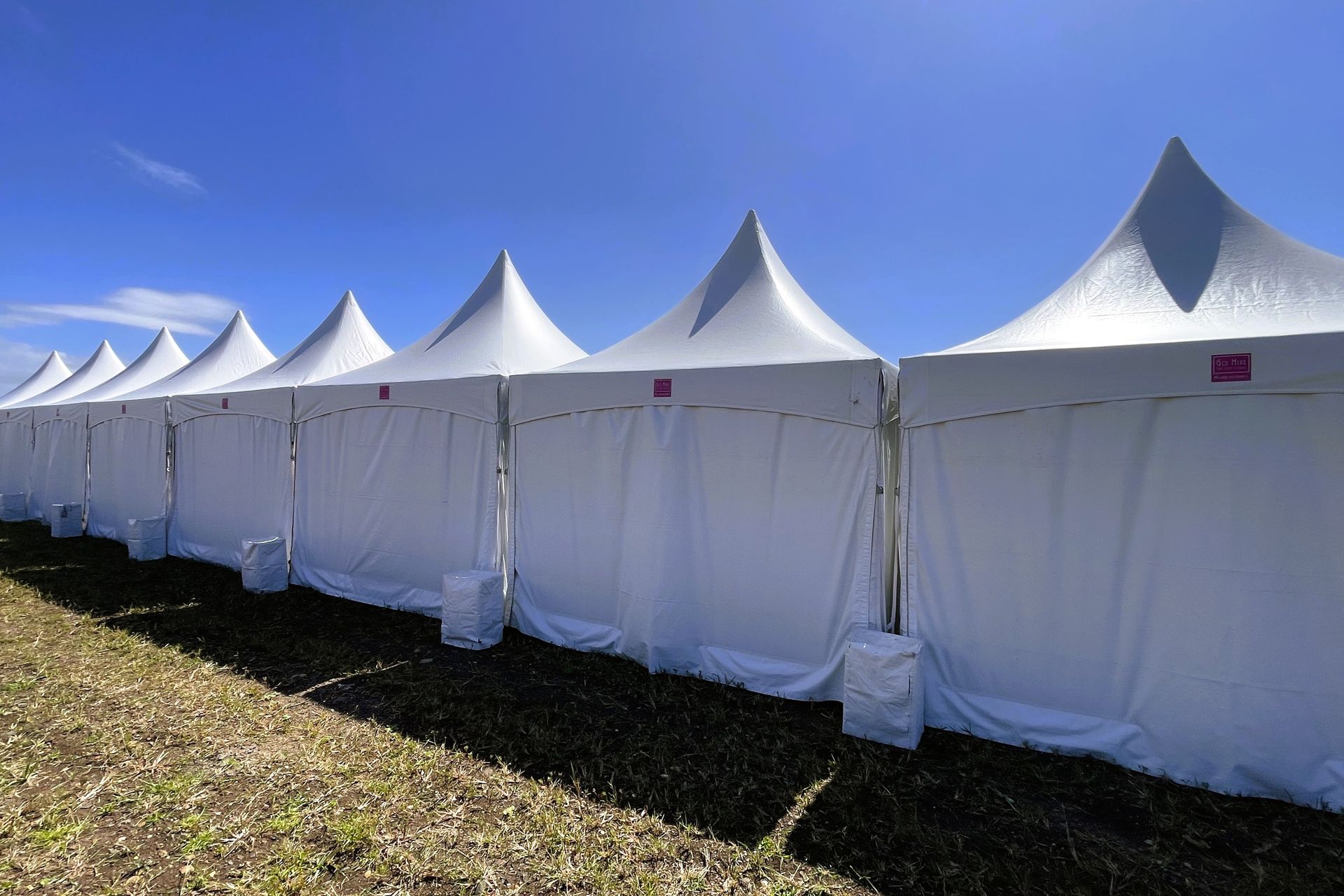A row of white tents are lined up in a field