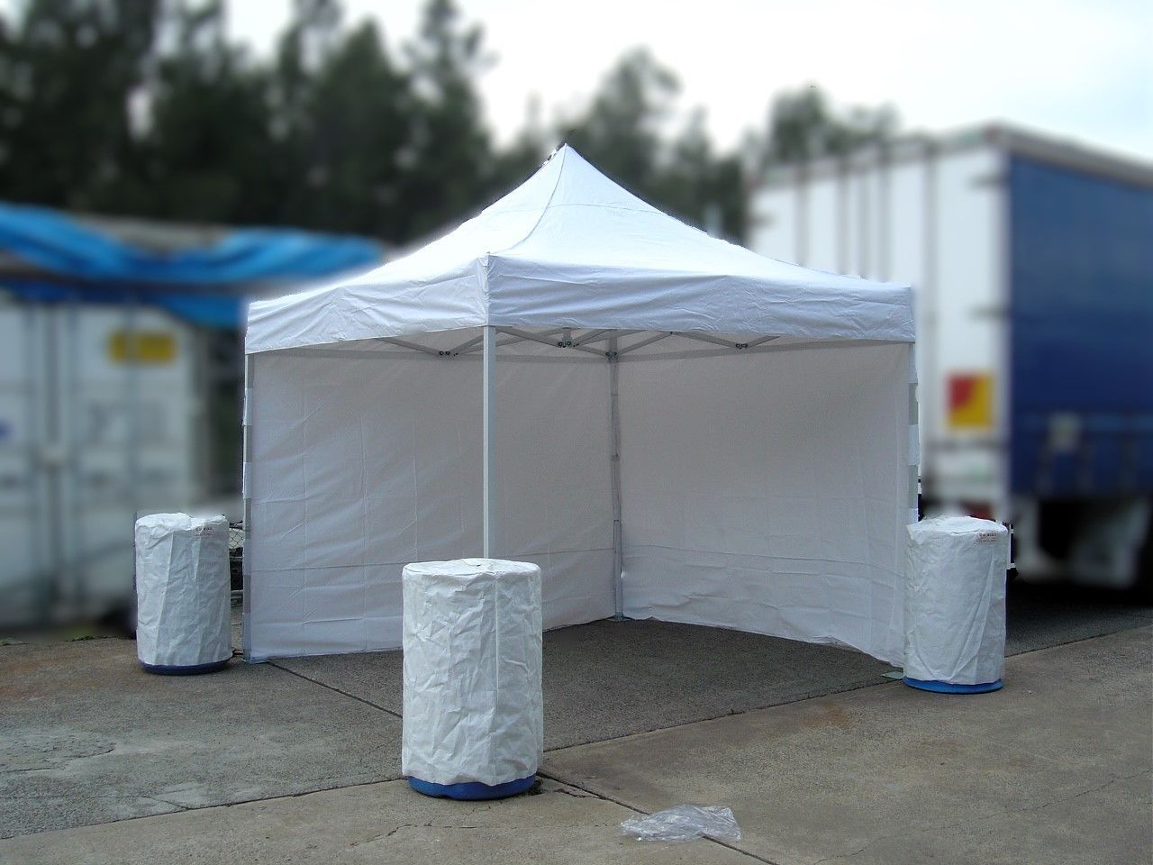 A white tent is sitting on the ground in front of a blue truck.