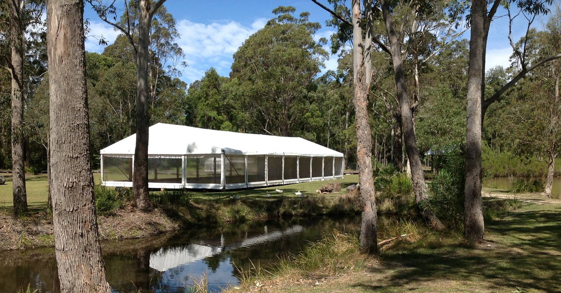 A white tent is sitting next to a pond in the middle of a forest.