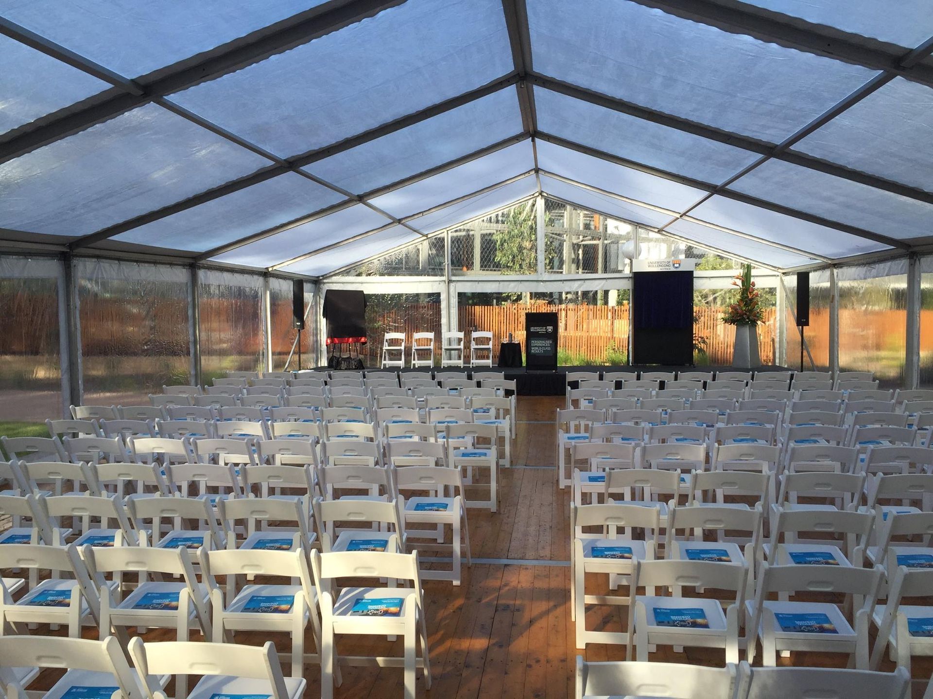 Rows of white chairs are lined up under a clear tent.