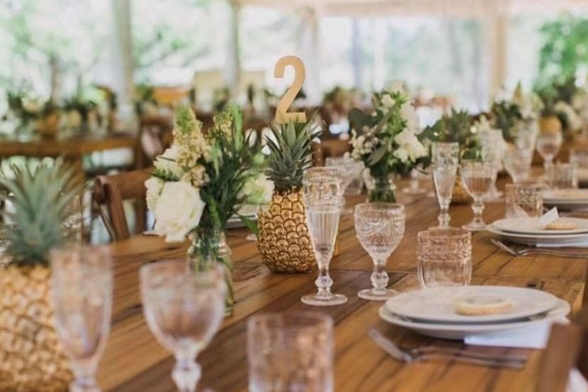 A long wooden table with plates , glasses , and pineapples on it.
