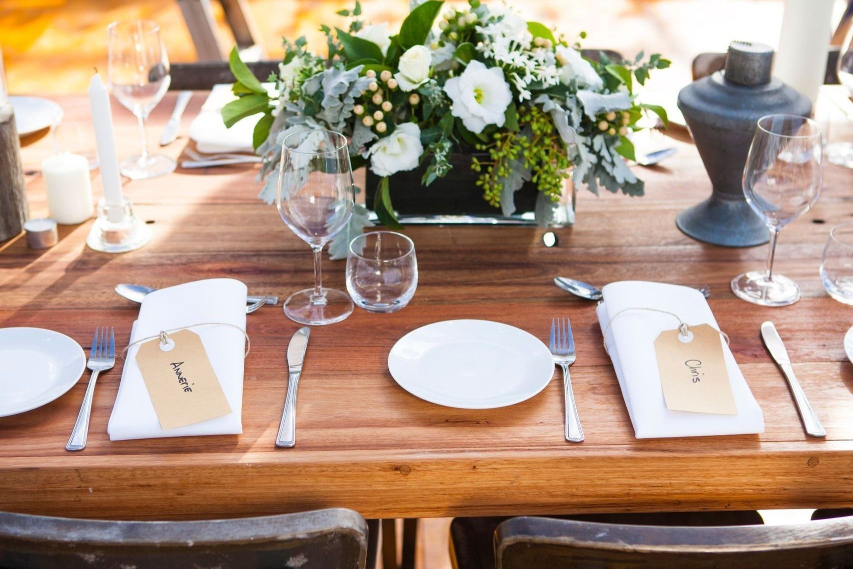 A wooden table with plates , utensils , and a vase of flowers on it.