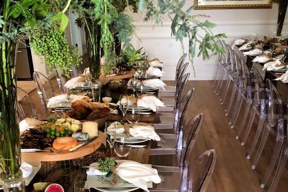 A long table with clear chairs and plates of food on it.