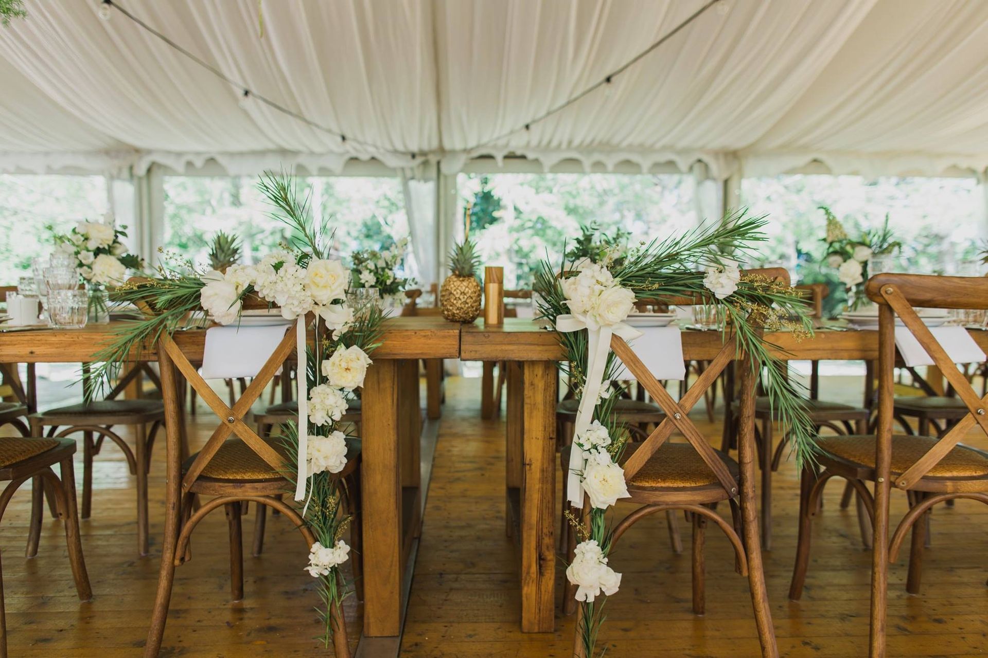 A long wooden table with flowers hanging from it in a tent.