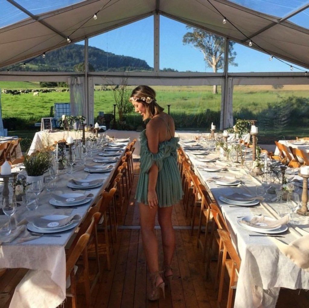 A woman in a green dress is standing in front of a long table set for a wedding reception.