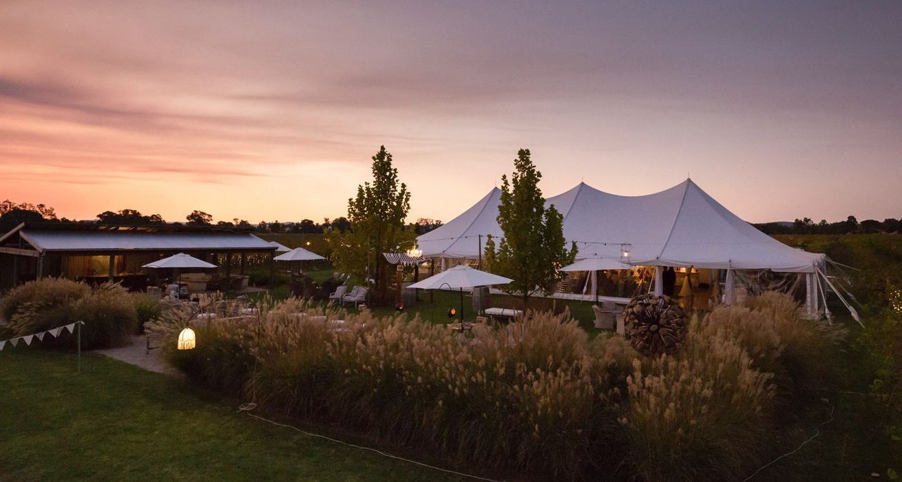 A large white tent is sitting in the middle of a field at sunset.