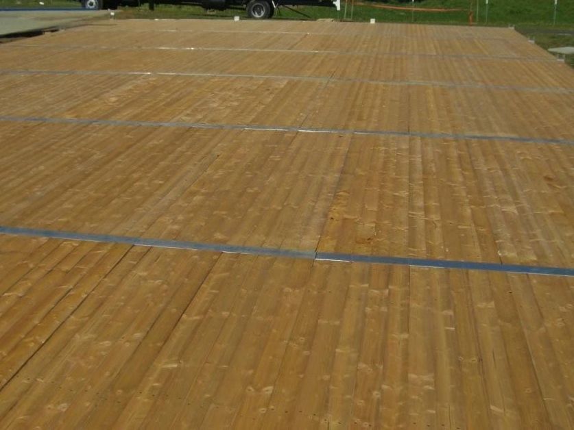 A large wooden dance floor is sitting in the middle of a field.