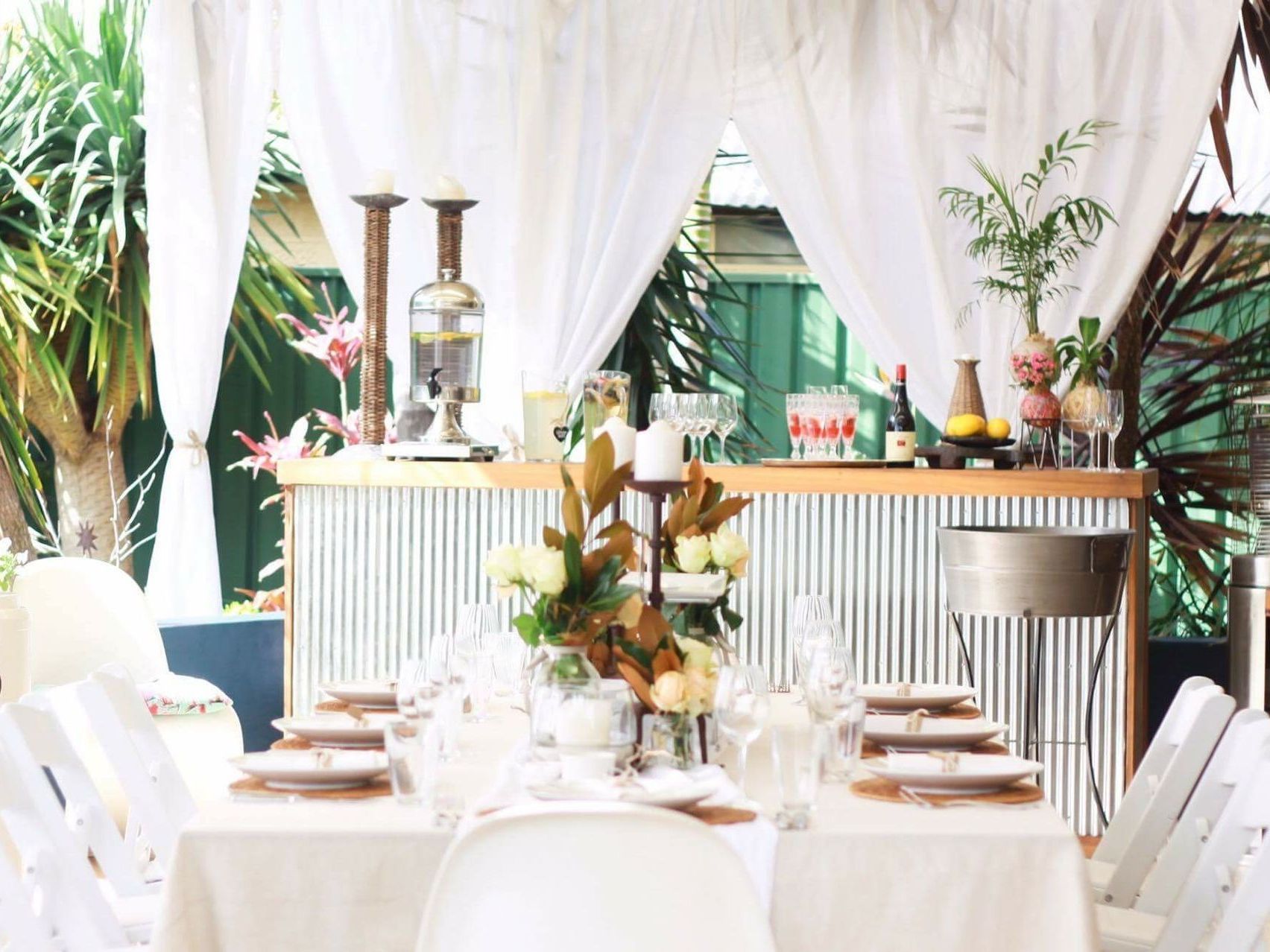 A table set for a party with white tables and chairs and a bar in the background.