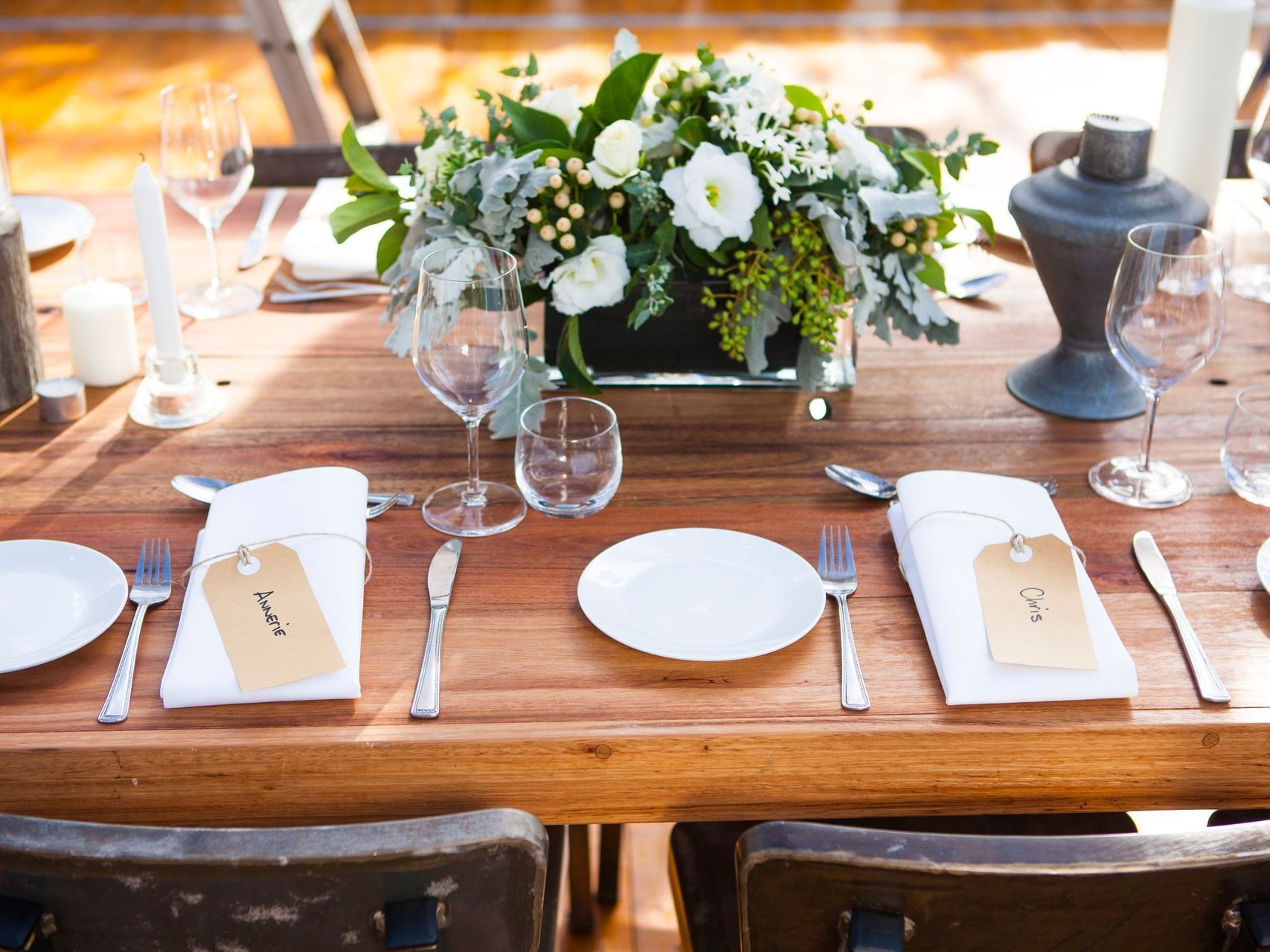 A wooden table with plates , utensils , and a vase of flowers on it.