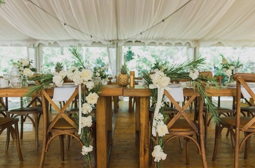 A long wooden table with white flowers on it in a tent.