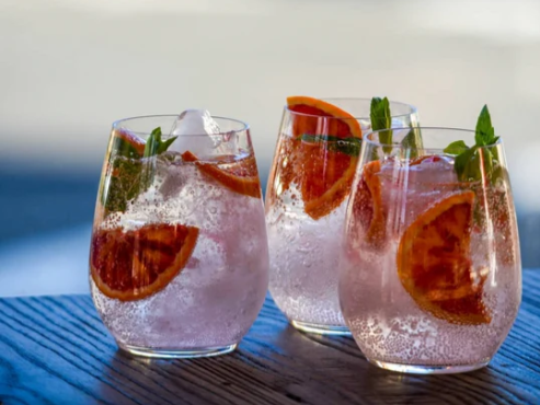 Three glasses of pink liquid with ice and orange slices on a wooden table.