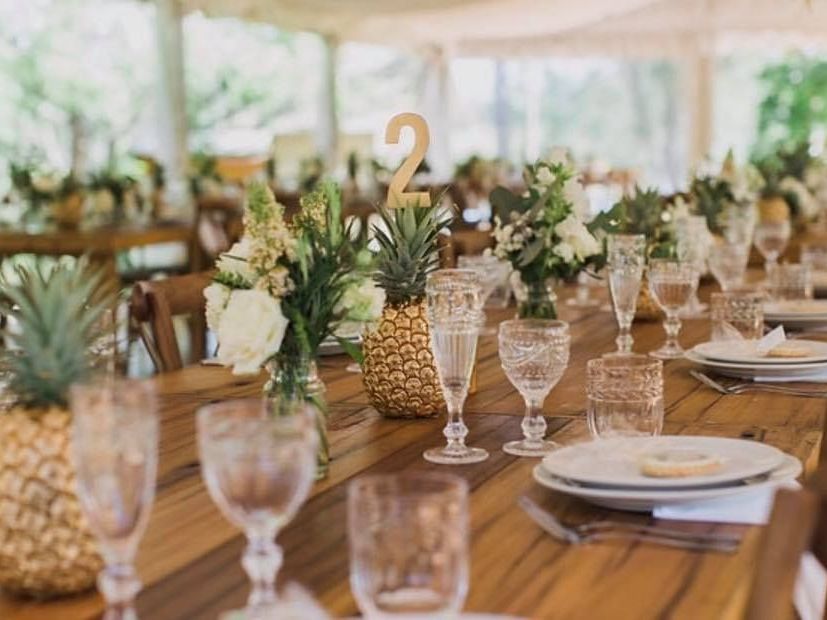 A long wooden table with plates , glasses , and pineapples on it.