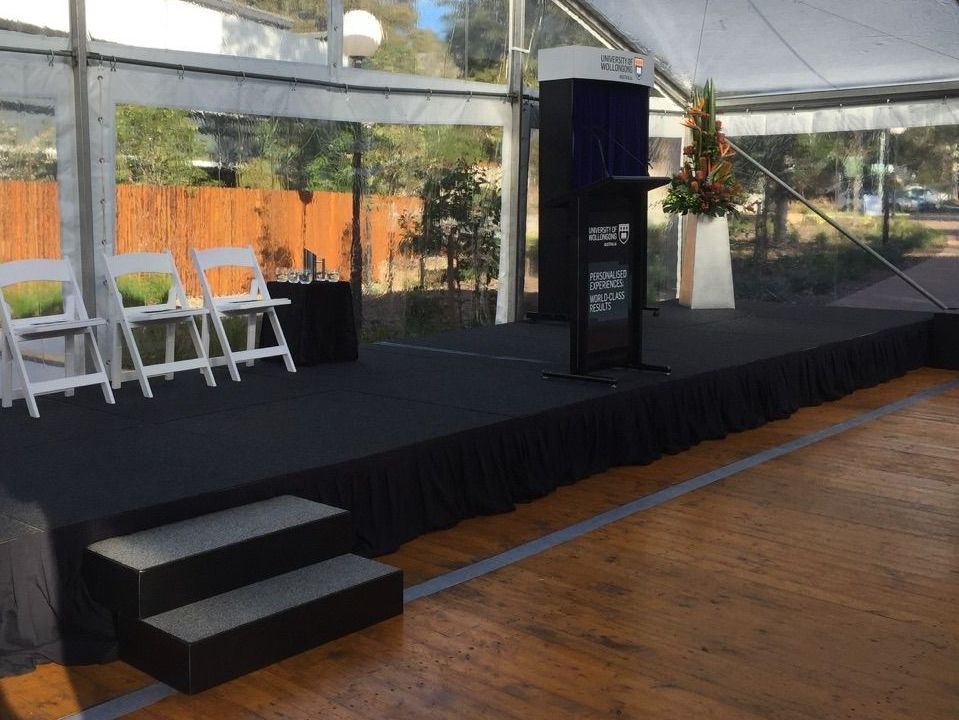 A stage with a podium and chairs under a tent.