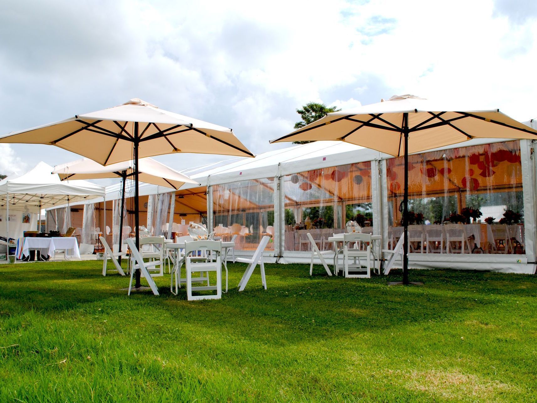 A row of tables and chairs under umbrellas in front of a tent.