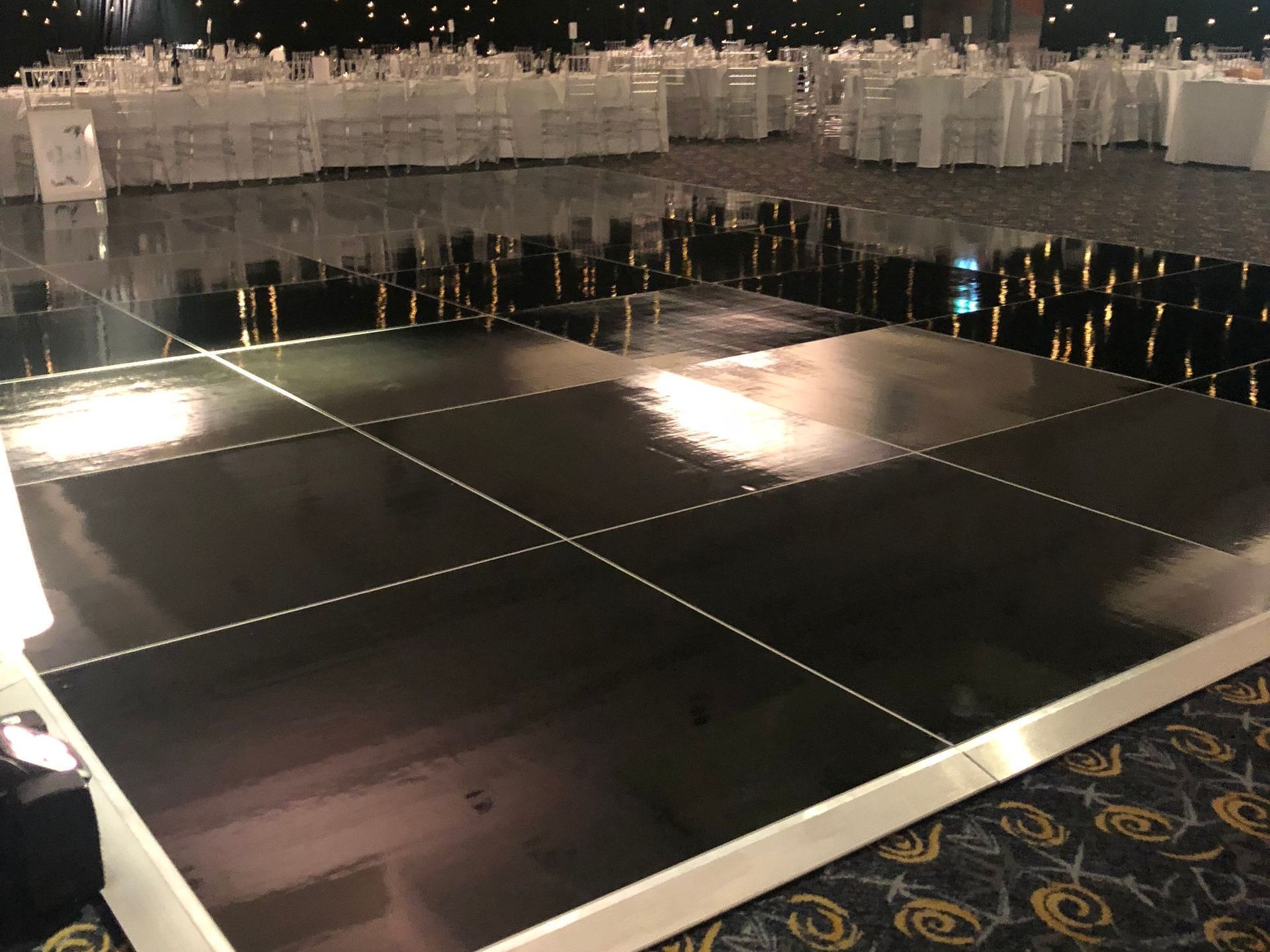 A black dance floor in a room with tables and chairs